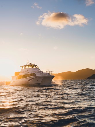 A Cougar Line boat cruises into Queen Charlotte Sound/Tōtaranui while the sun rises behind it in the Marlborough Sounds, New Zealand