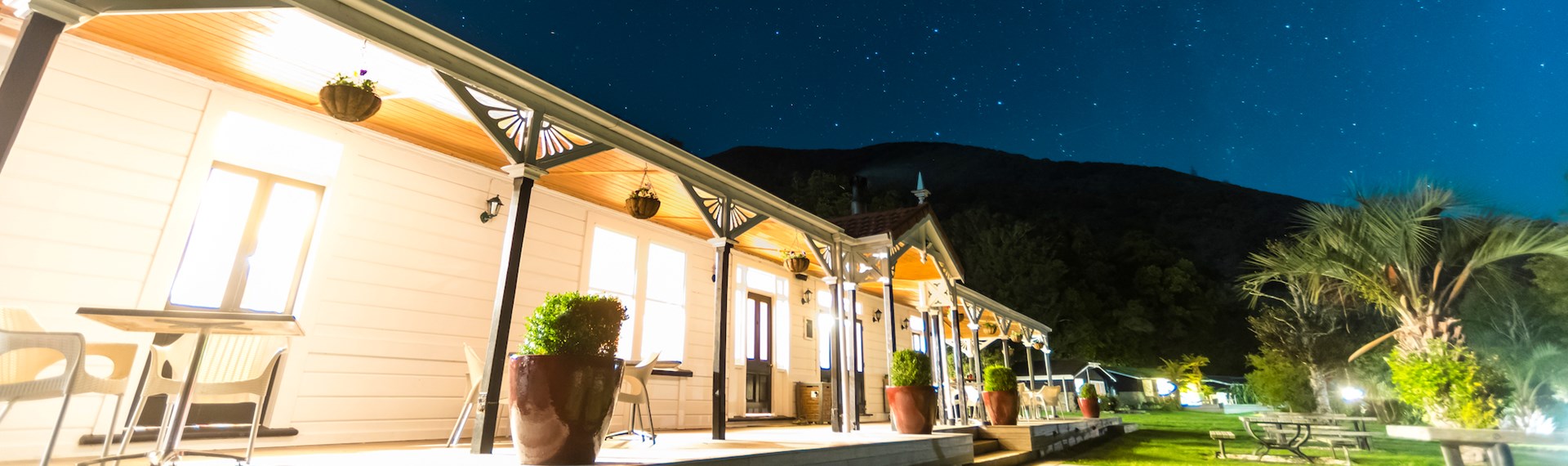 A view at night along the verandah of historic Howden House with lights on and stars in the sky, in the Marlborough Sounds at the top of New Zealand's South Island.